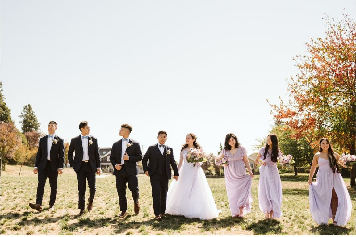 Wedding party holding flower bouquets standing outdoors with a bride and groom in the center.