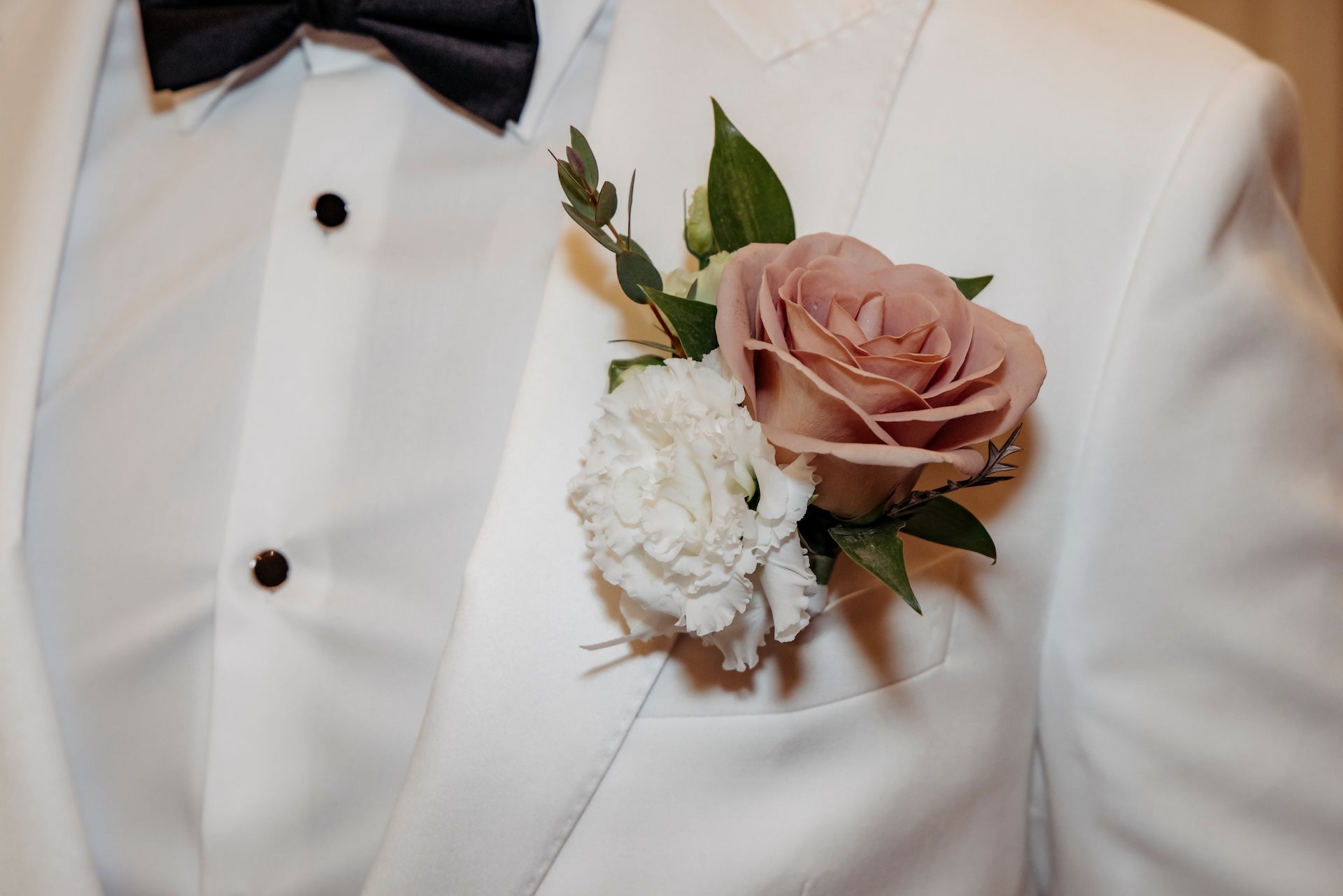 White tuxedo with a pink and white floral boutonniere on a light background