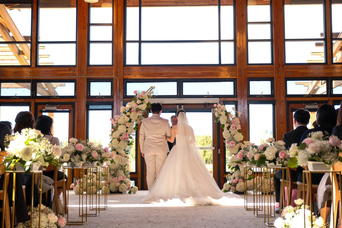 Romantic blush pink and white wedding ceremony arch with floral aisle arrangements at Riverway Clubhouse in Burnaby by Burst Flowers.