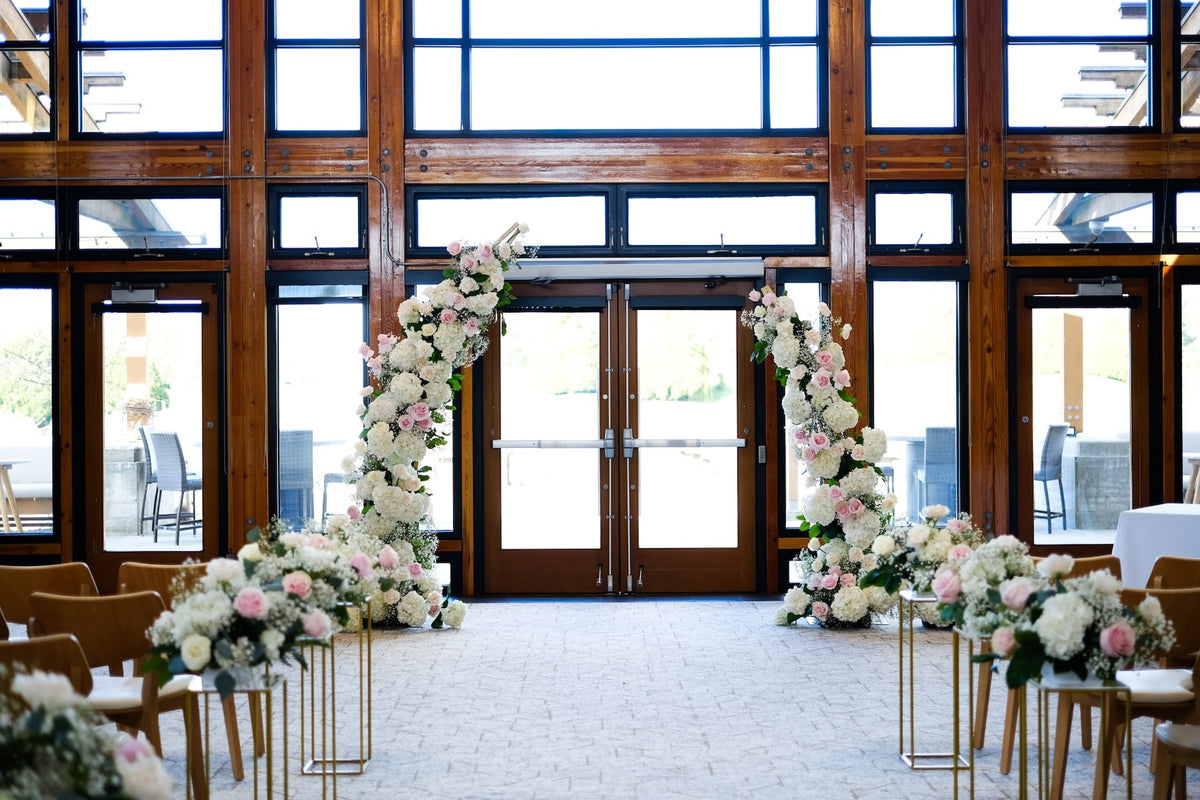 Romantic blush pink and white wedding ceremony arch with floral aisle arrangements at Riverway Clubhouse in Burnaby by Burst Flowers.