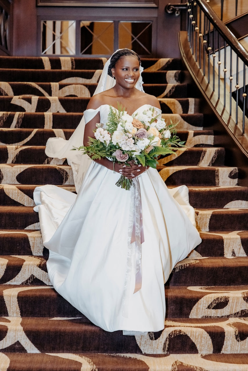 Bride in a white wedding dress holding a bouquet on a decorative staircase at TCC.
