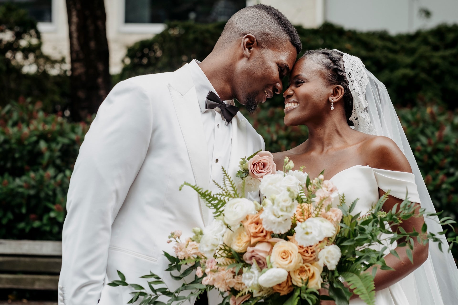 Couple on their wedding day with a bouquet of flowers, standing outdoors.