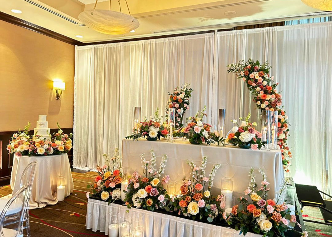 Decorated wedding setup with floral arch, head table floral arrangements, cake table arrangements and candles in a room.