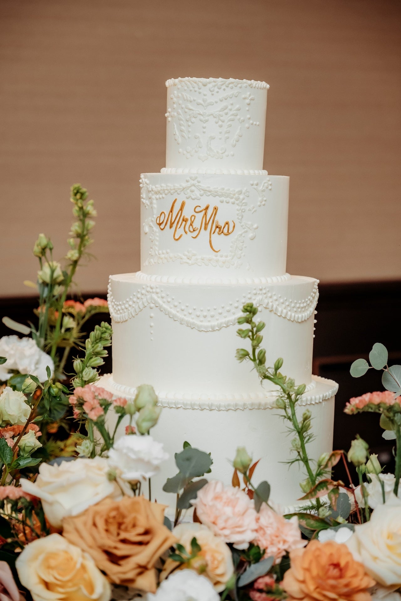 White wedding cake with 'Mr & Mrs' inscription, surrounded by flowers on a blurred background
