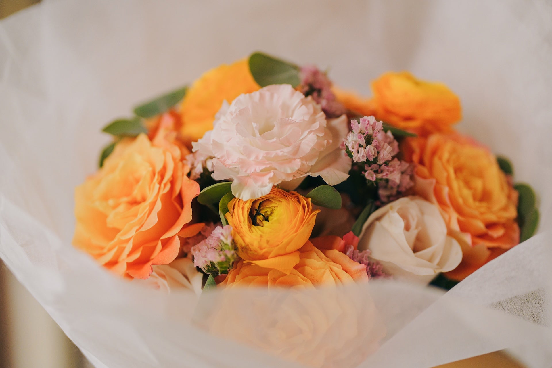 Bouquet of orange and pink flowers with green leaves on a white background