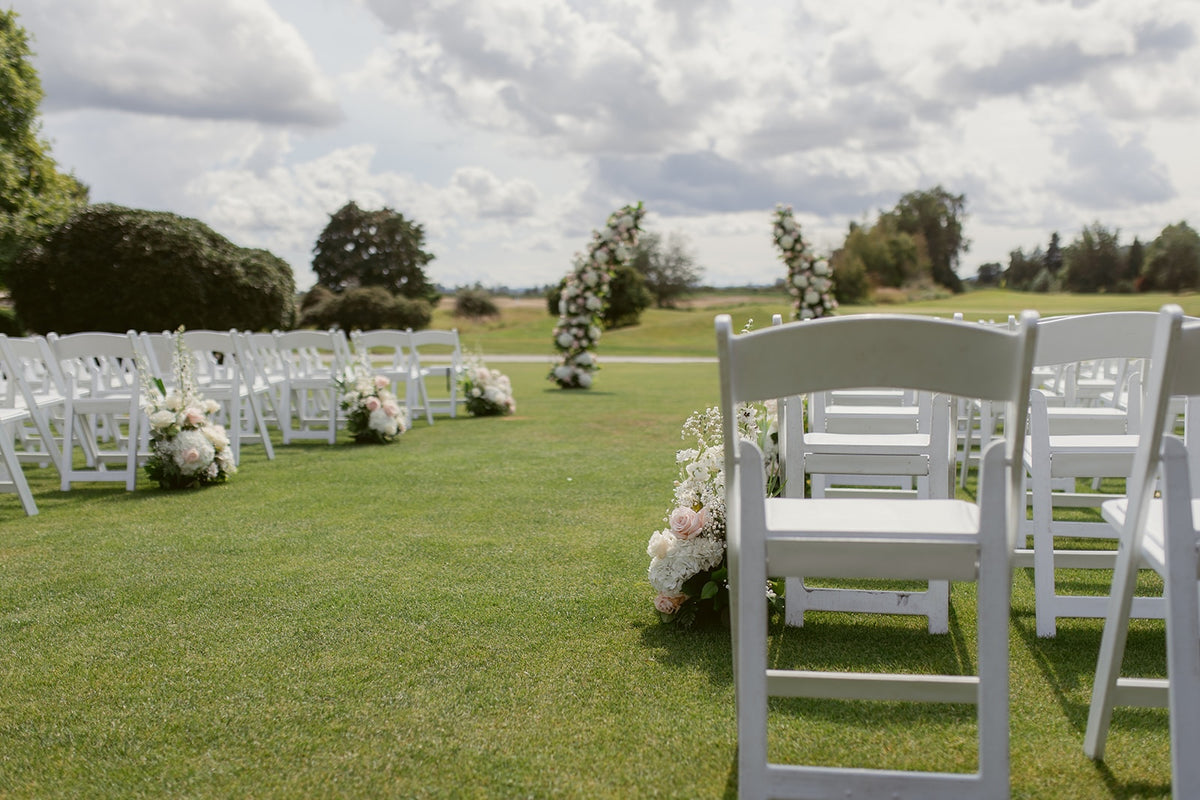 Outdoor wedding ceremony at Swaneset in Pitt Meadows with two floral arch columns and blush white aisle flowers.