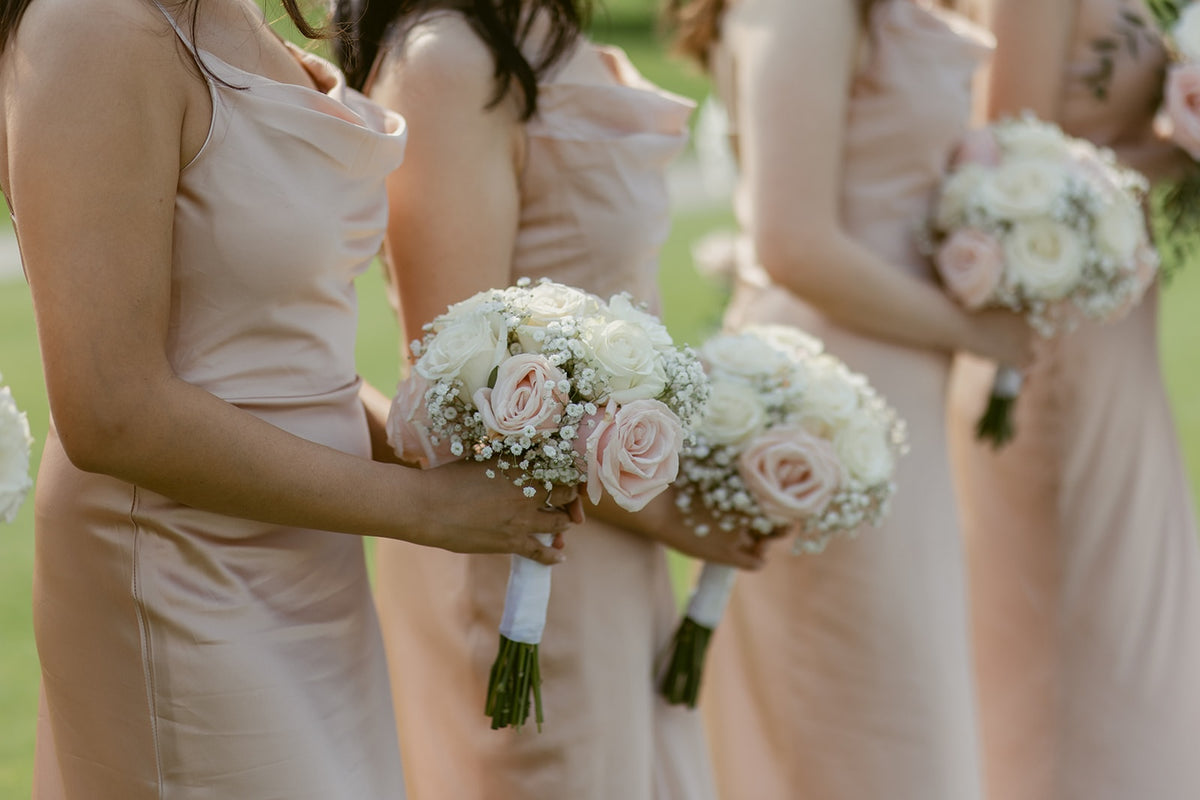 Bridesmaids in blush pink dresses holding romantic white and pale pink rose bouquets with baby's breath at Swaneset.