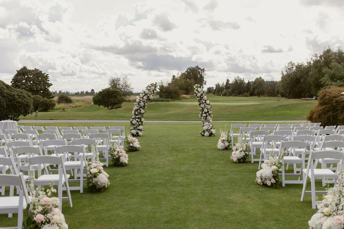 Outdoor wedding ceremony at Swaneset in Pitt Meadows with two floral arch columns and blush white aisle flowers.