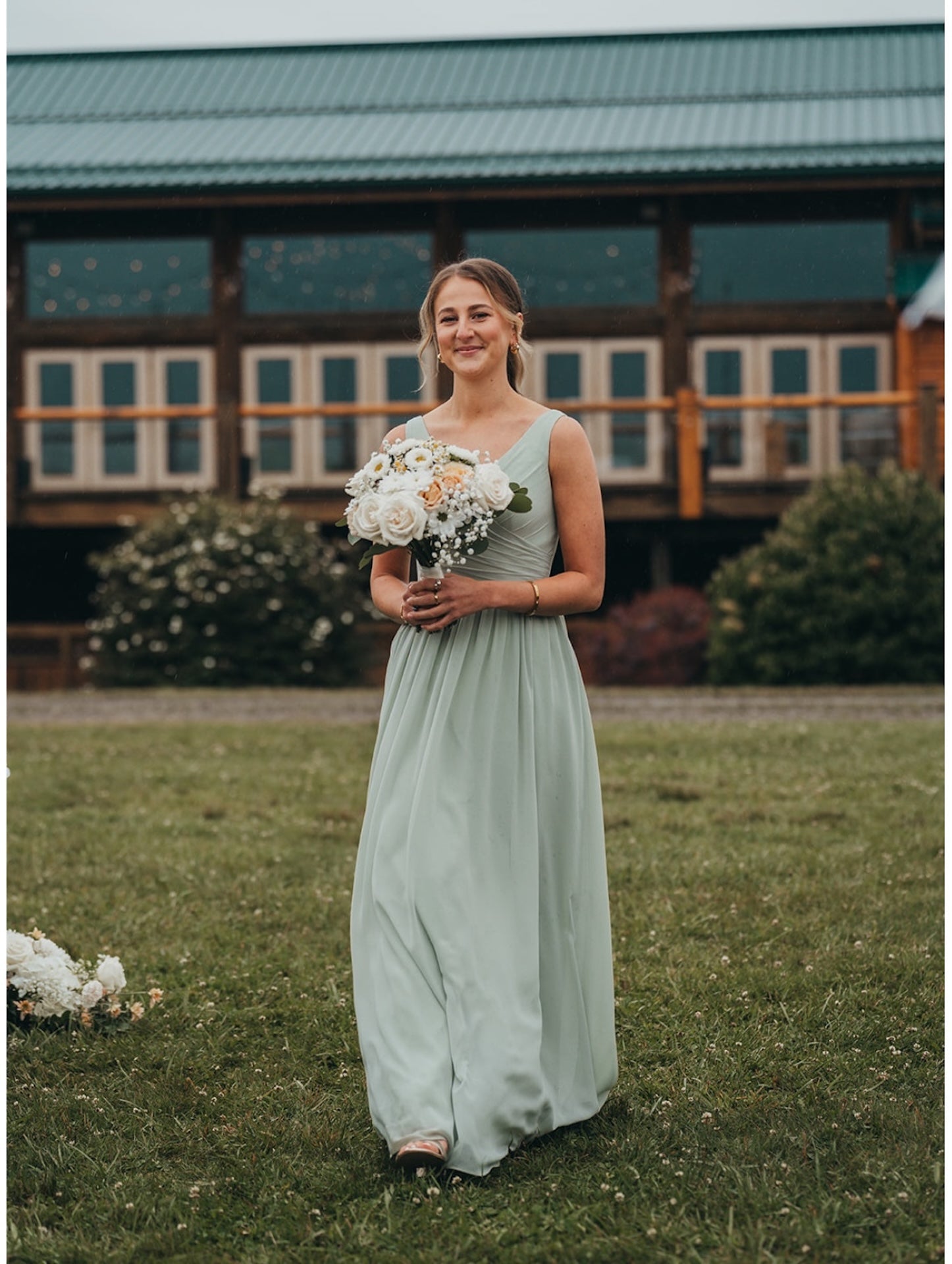 A bridesmaid in a long light green dress holding a bouquet of flowers outdoors.