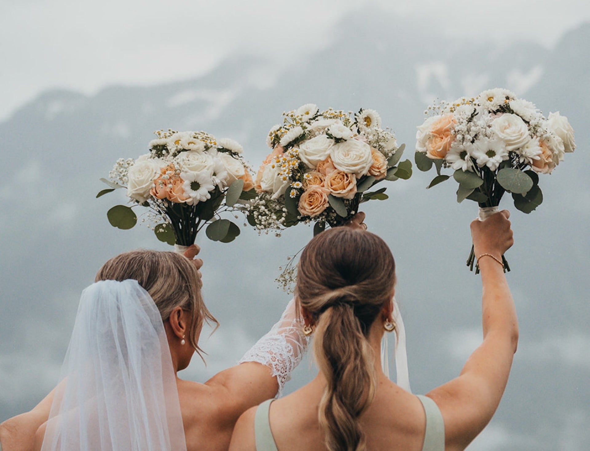 a bride and two bridesmaids holding bouquets of flowers with a mountainous background