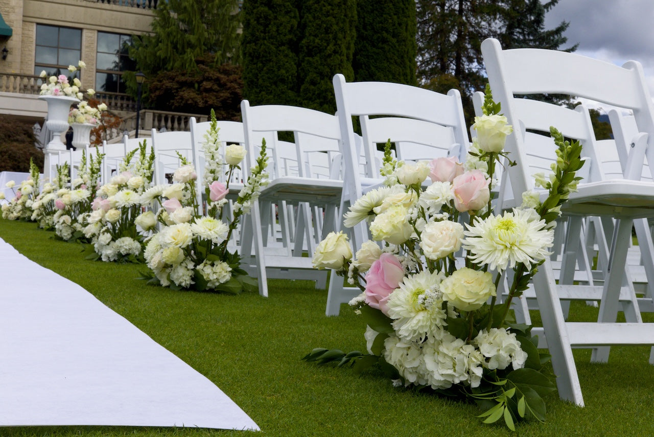 Decorative aisle floral arrangements on a grassy area with white chairs and a white aisle runner at Swaneset Bay Resort & Country Club.