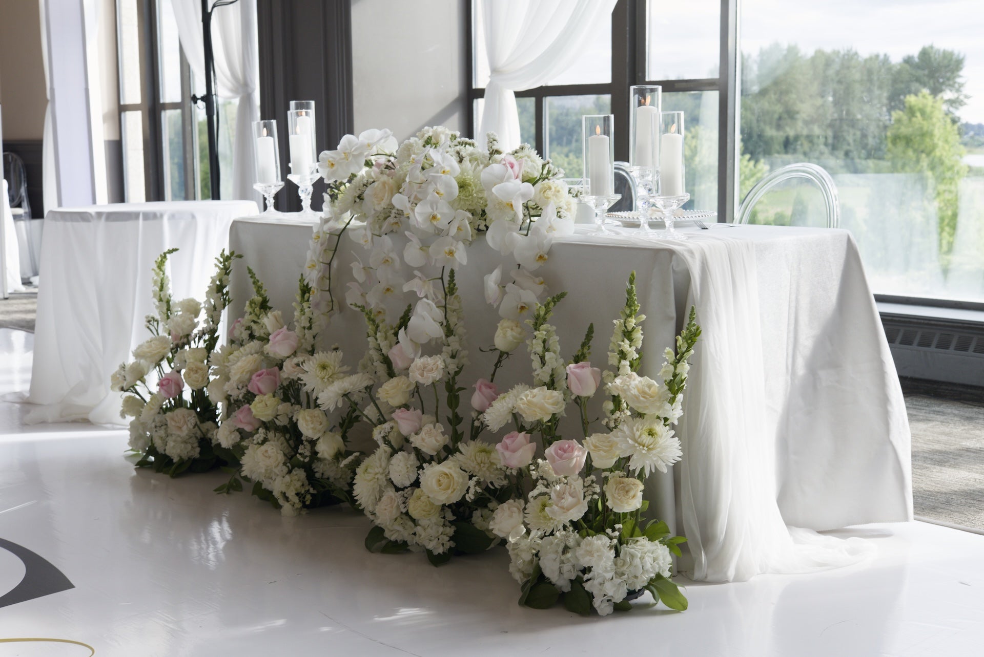 Decorative white and light pink wedding floral arrangements on a head table with a white tablecloth in at Swaneset Bay Resort & Country Club grand ball room.