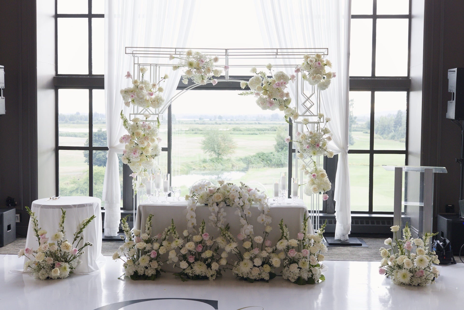 Decorative floral arch with flowers on a  head table in a room with large windows at Swaneset Bay Resort & Country Club.