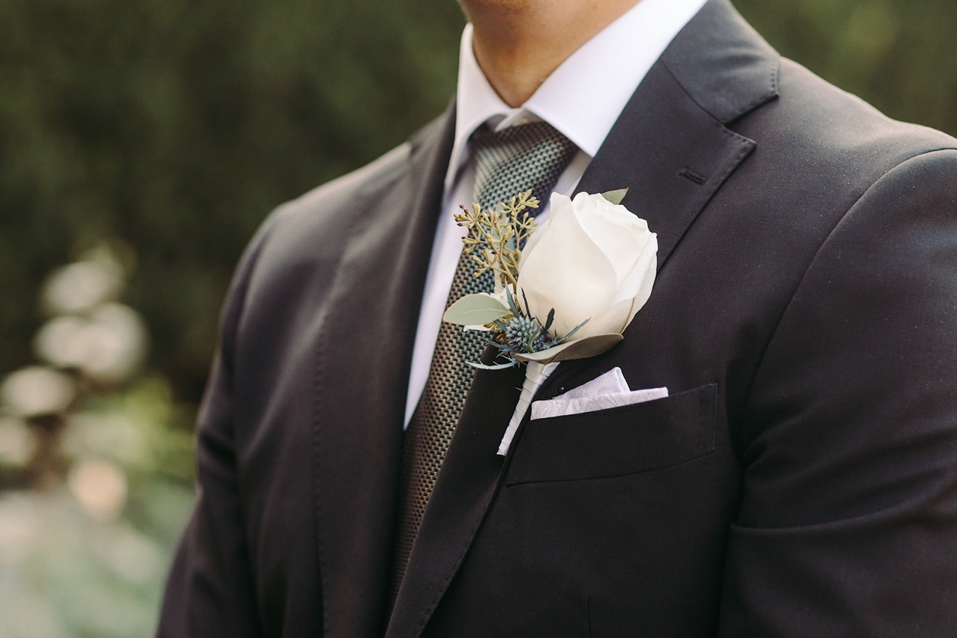 Man wearing a dark suit with a white rose boutonniere and green tie.