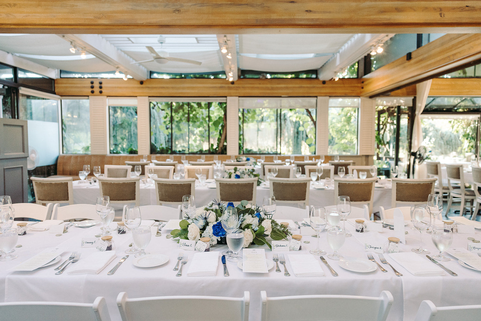 Dining hall with tables set for table arrangements,  large windows, and wooden beams.