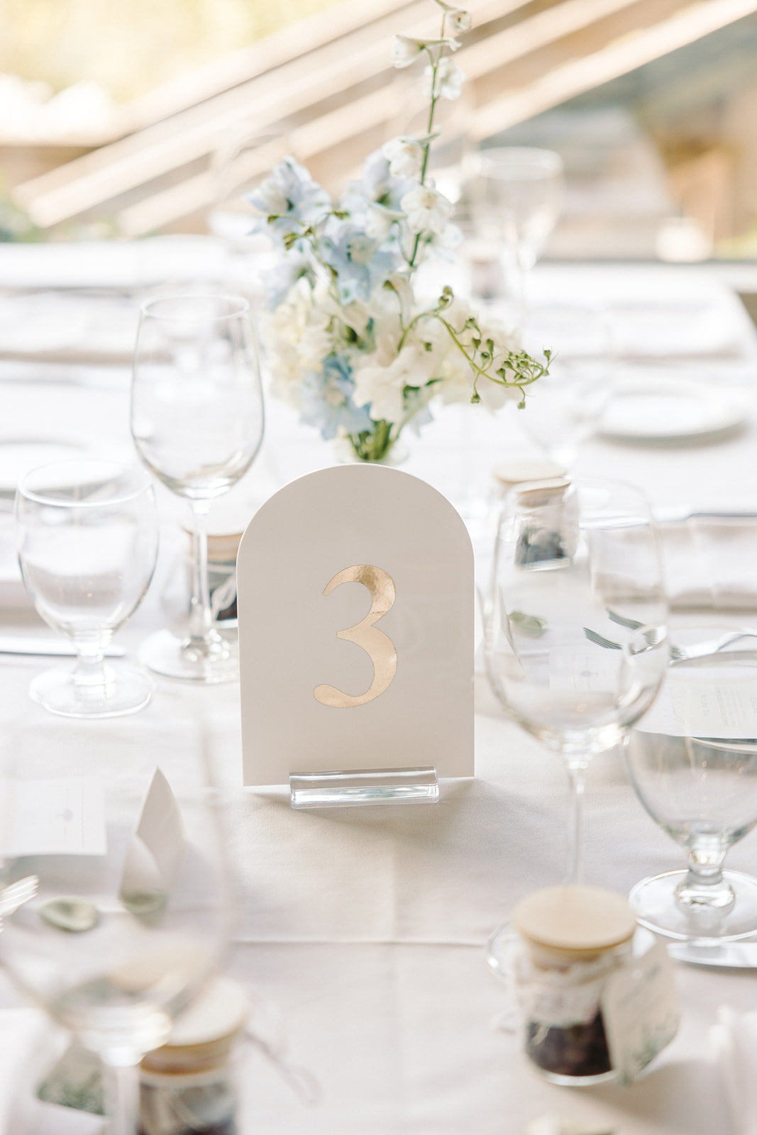 Table setting with a floral bud vase and a table number card on a white tablecloth.