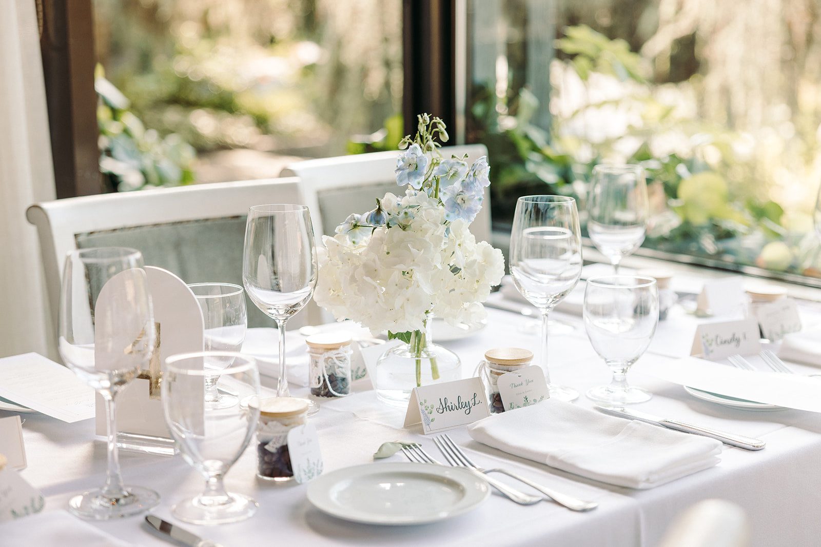 Elegant table setting with white tablecloth, glasses, and floral centerpiece.