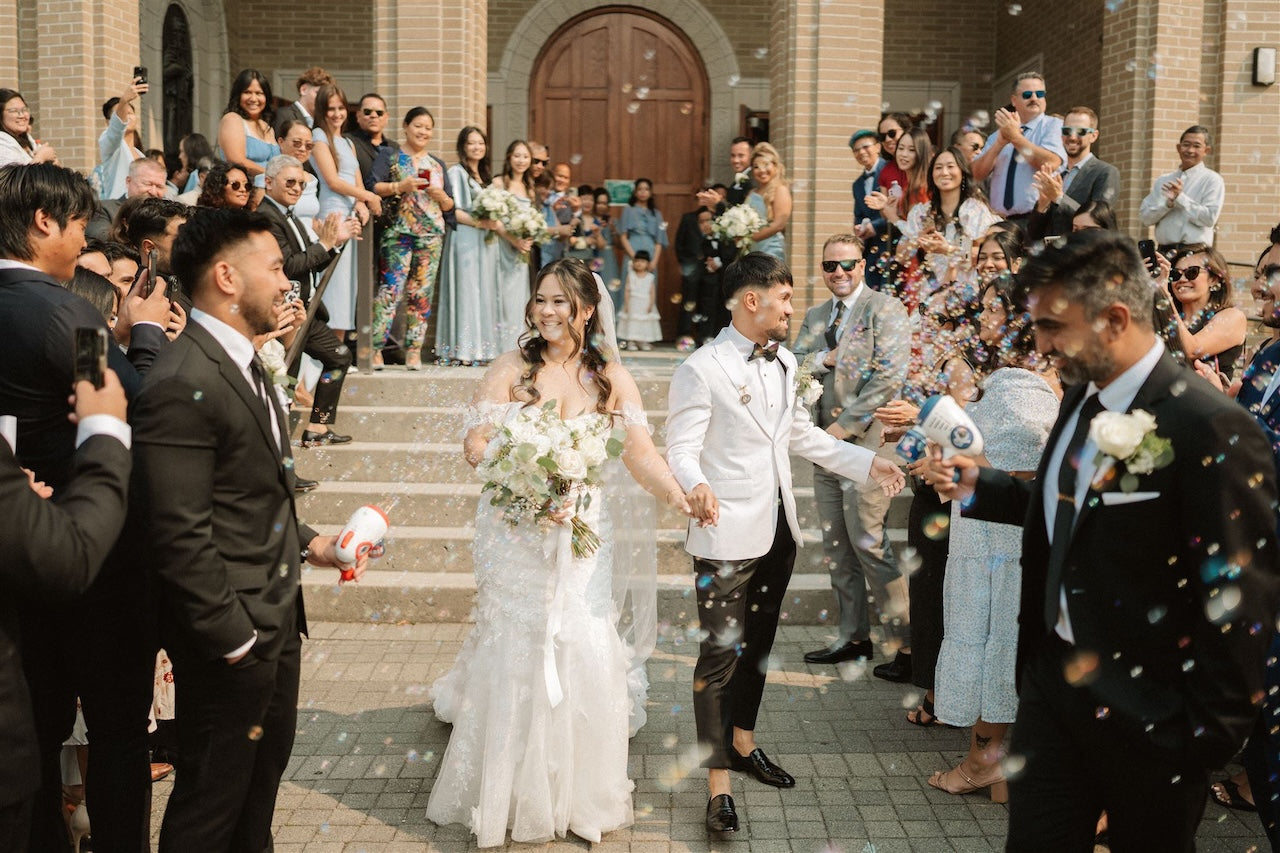 Wedding ceremony with bride and groom walking down steps, surrounded by guests and confetti.